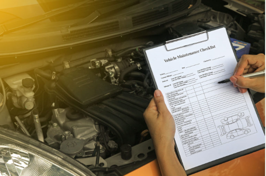 Vehicle maintenance checklist held in front of an open engine bay